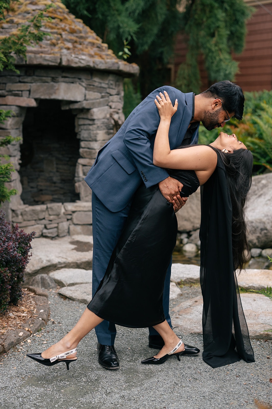 Piyush dips Priyanka in a playful pose beside the outdoor stone fireplace at Willows Lodge in Woodinville