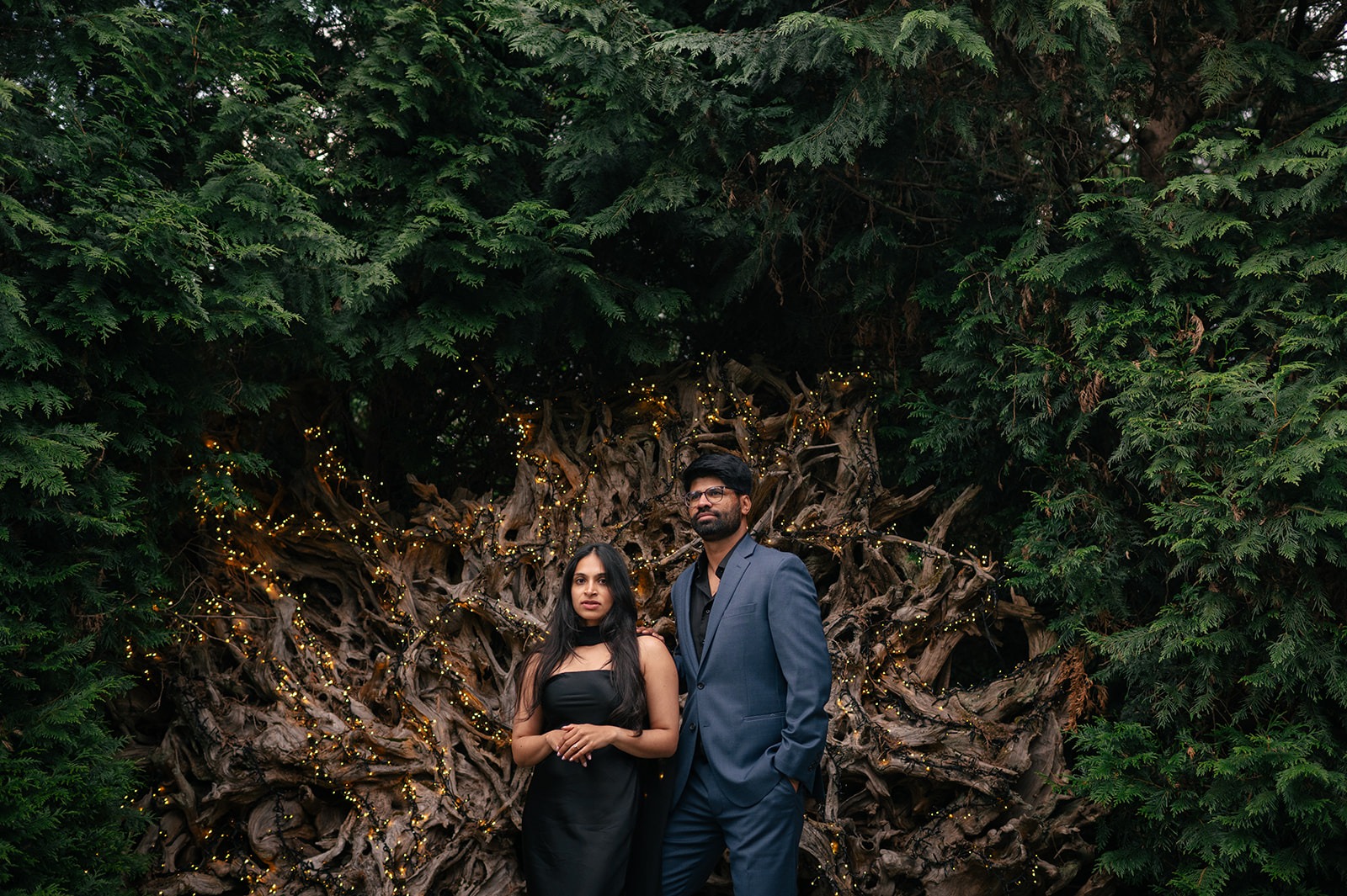 Piyush and Priyanka pose in front of the dramatic driftwood and twinkle-light installation in the gardens at Willows Lodge in Woodinville, WA