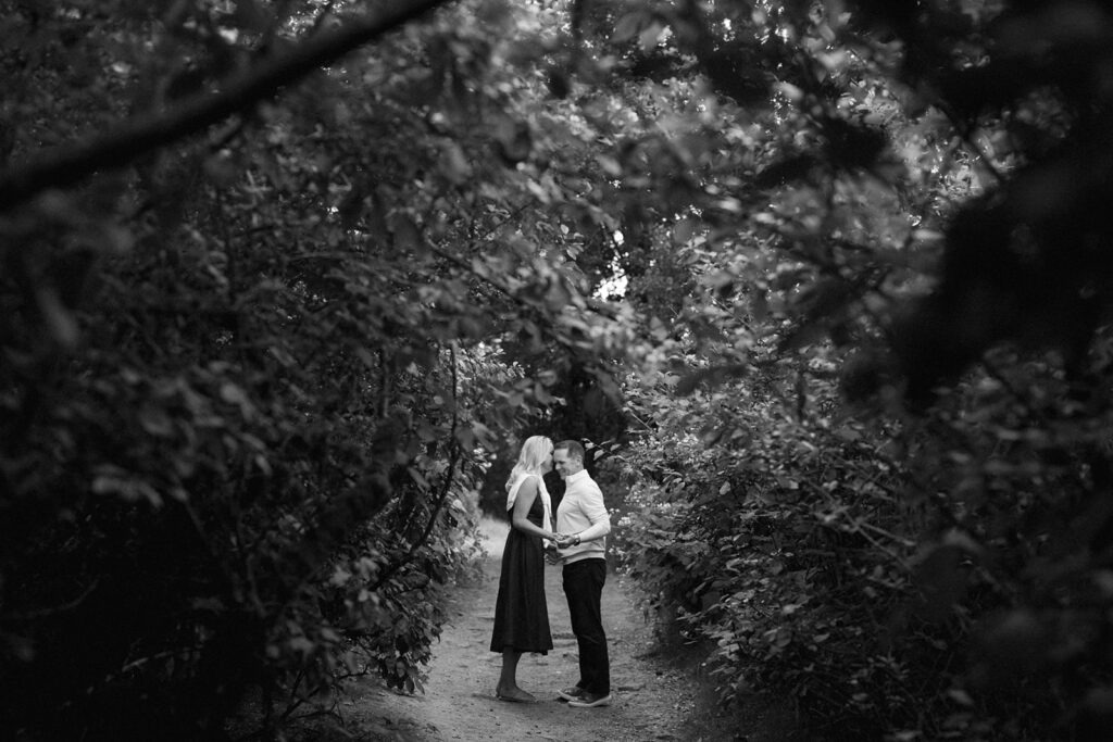 A black-and-white photo captures a quiet moment from this field engagement session under a leafy archway