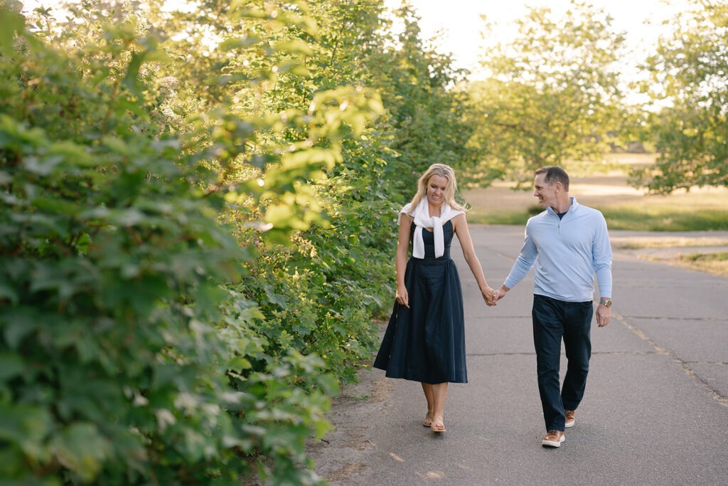 Couple walks hand in hand along a paved path beside a tall hedge