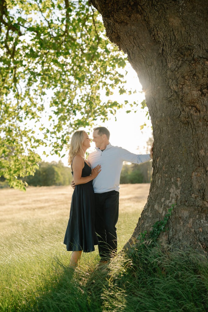 Couple embraces beneath the trunk of a large oak tree