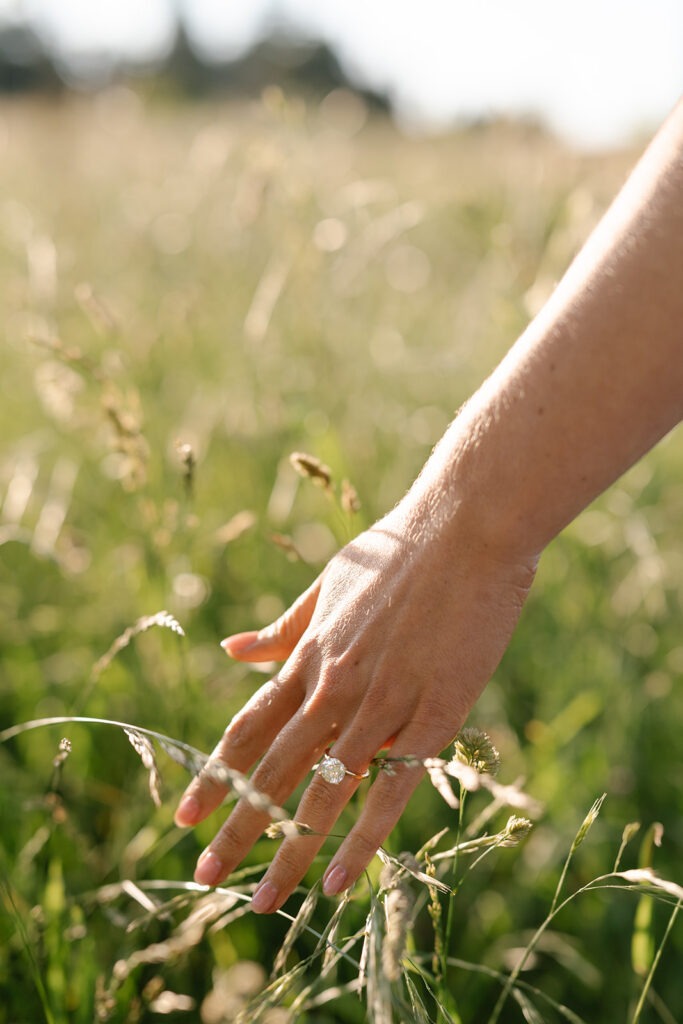 Close-up from the field engagement session showing a hand reaching into tall grass, ring catching the light