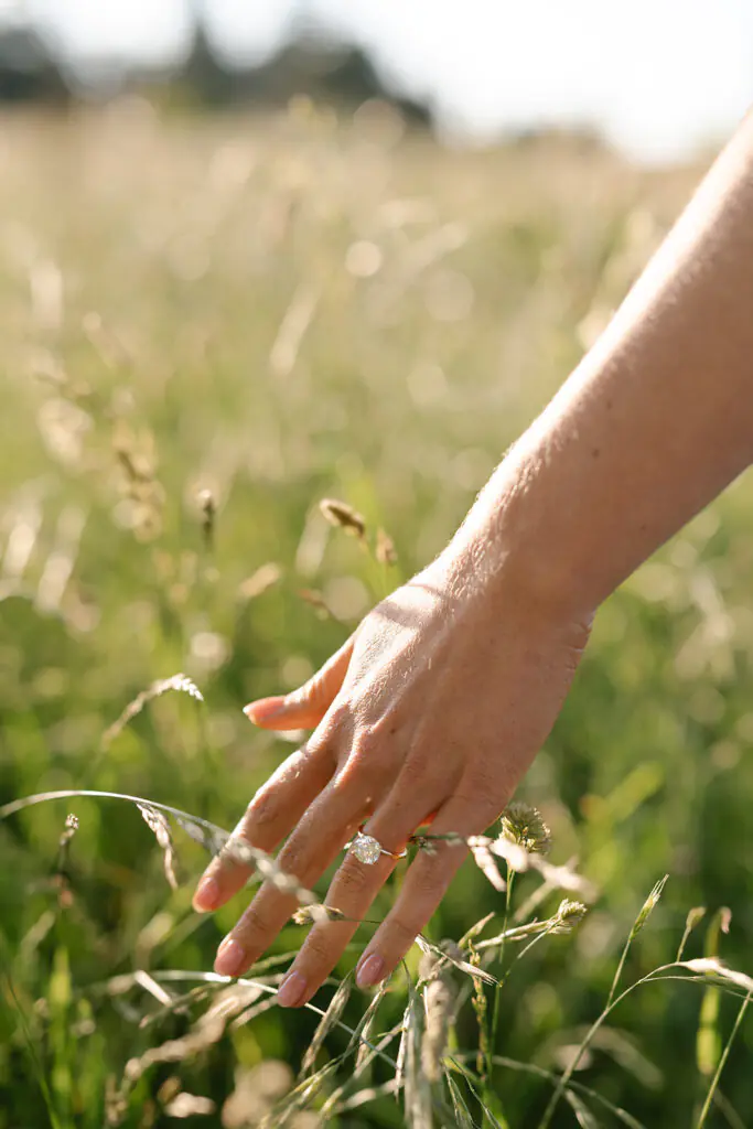 Close-up from the field engagement session showing a hand reaching into tall grass, ring catching the light