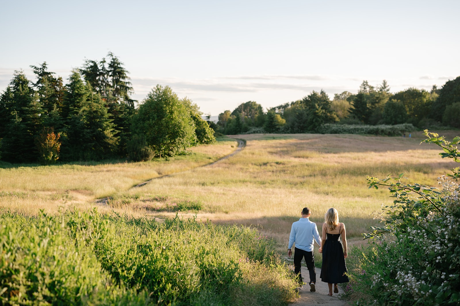 Couple walks away down a dirt path through the grassy field at Discovery Park, seen from a distance