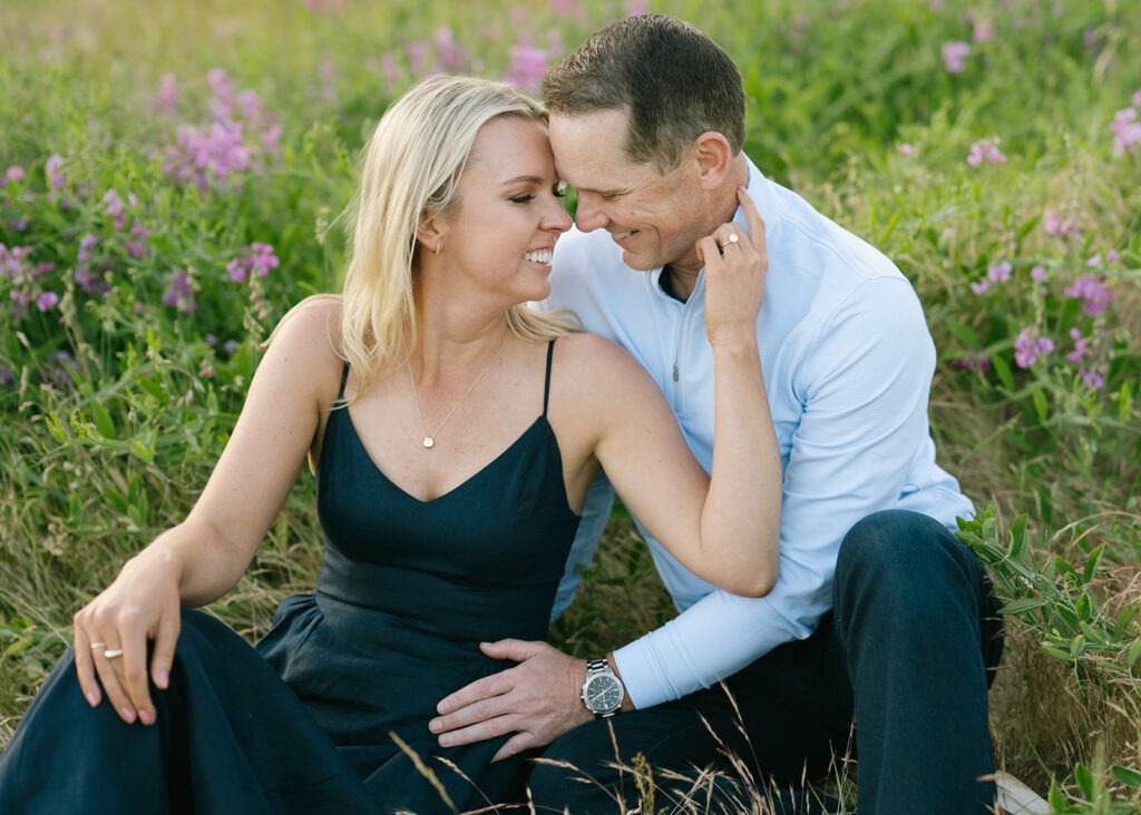 This field engagement session winds down with the couple sitting close in the wildflowers, smiling