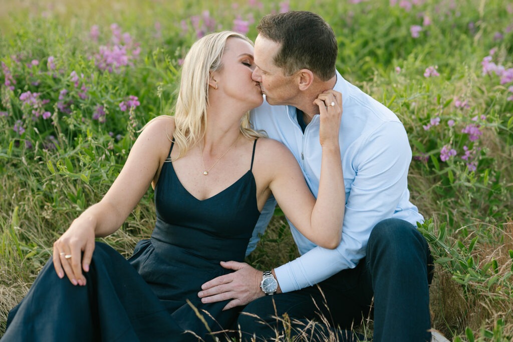 Couple kisses while sitting together in the purple wildflower field