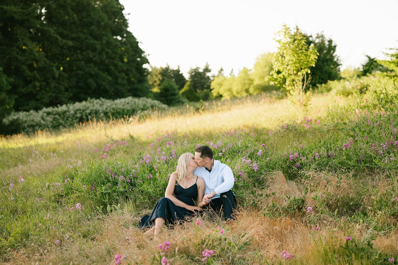 Wide view of the couple sitting together in the wildflower field as evening light settles in