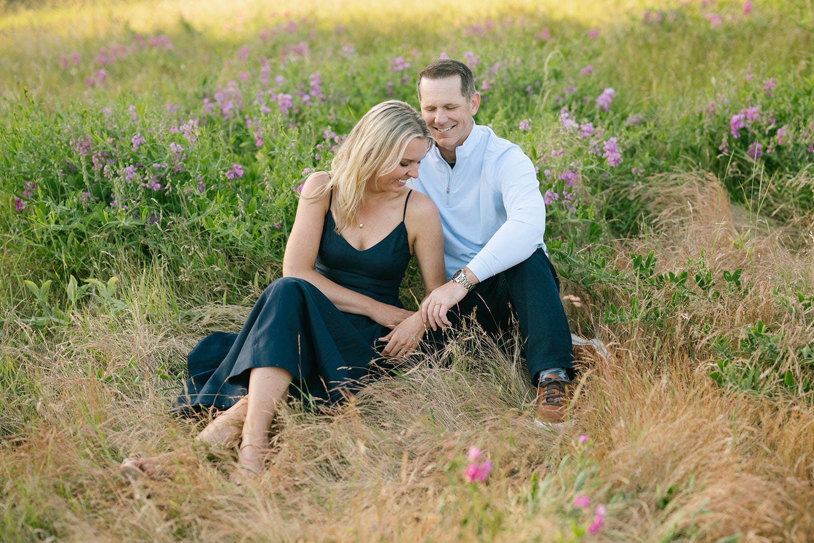 Couple sits close together in a field of purple wildflowers