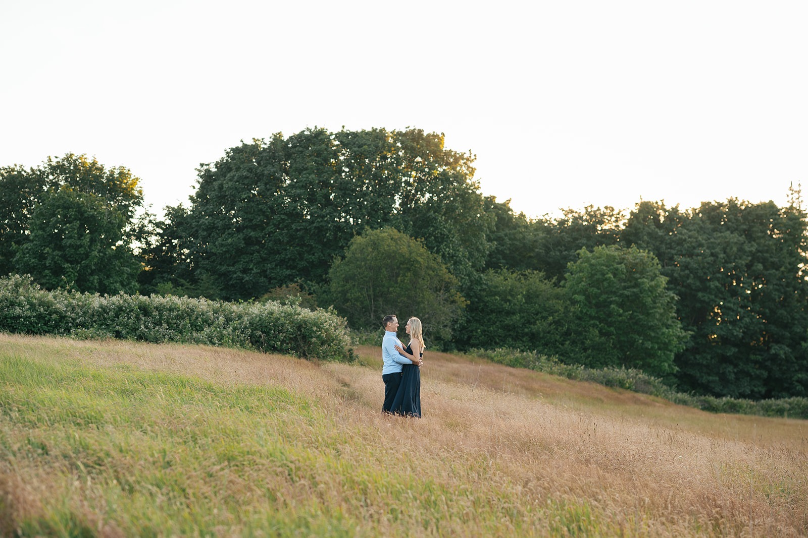Couple embraces on a golden grassy hillside, seen from a distance