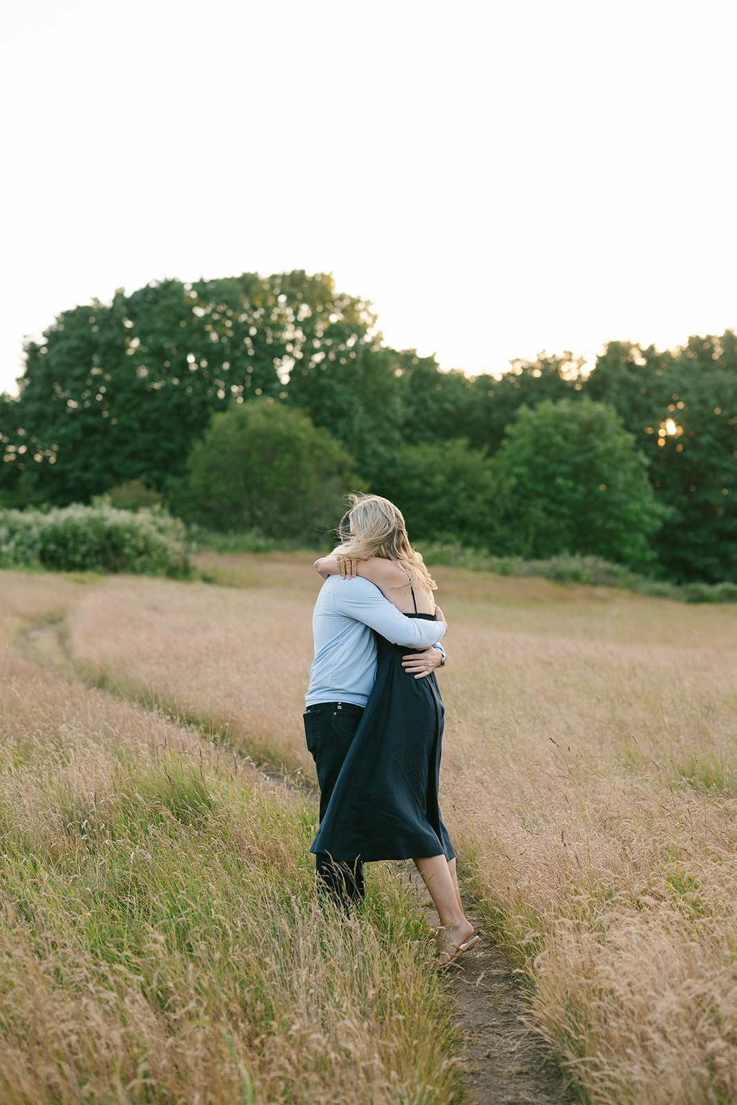 Couple embraces while walking together down a grassy path