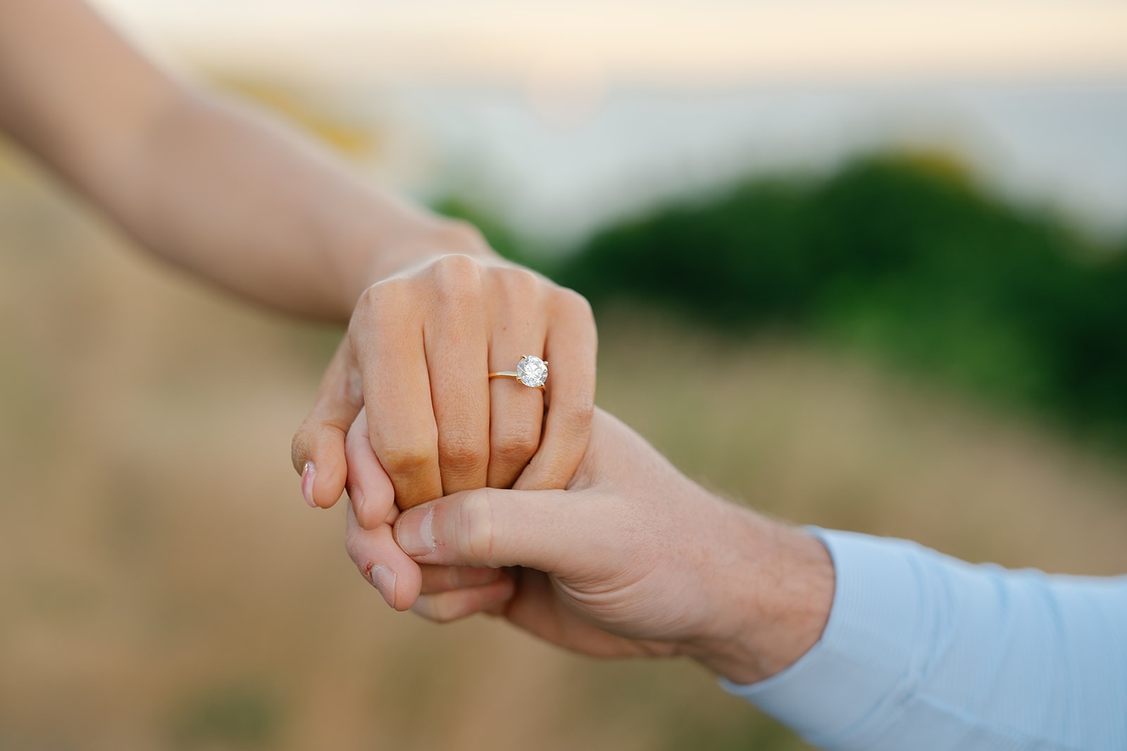 Close-up of clasped hands showing an engagement ring, water blurred behind them