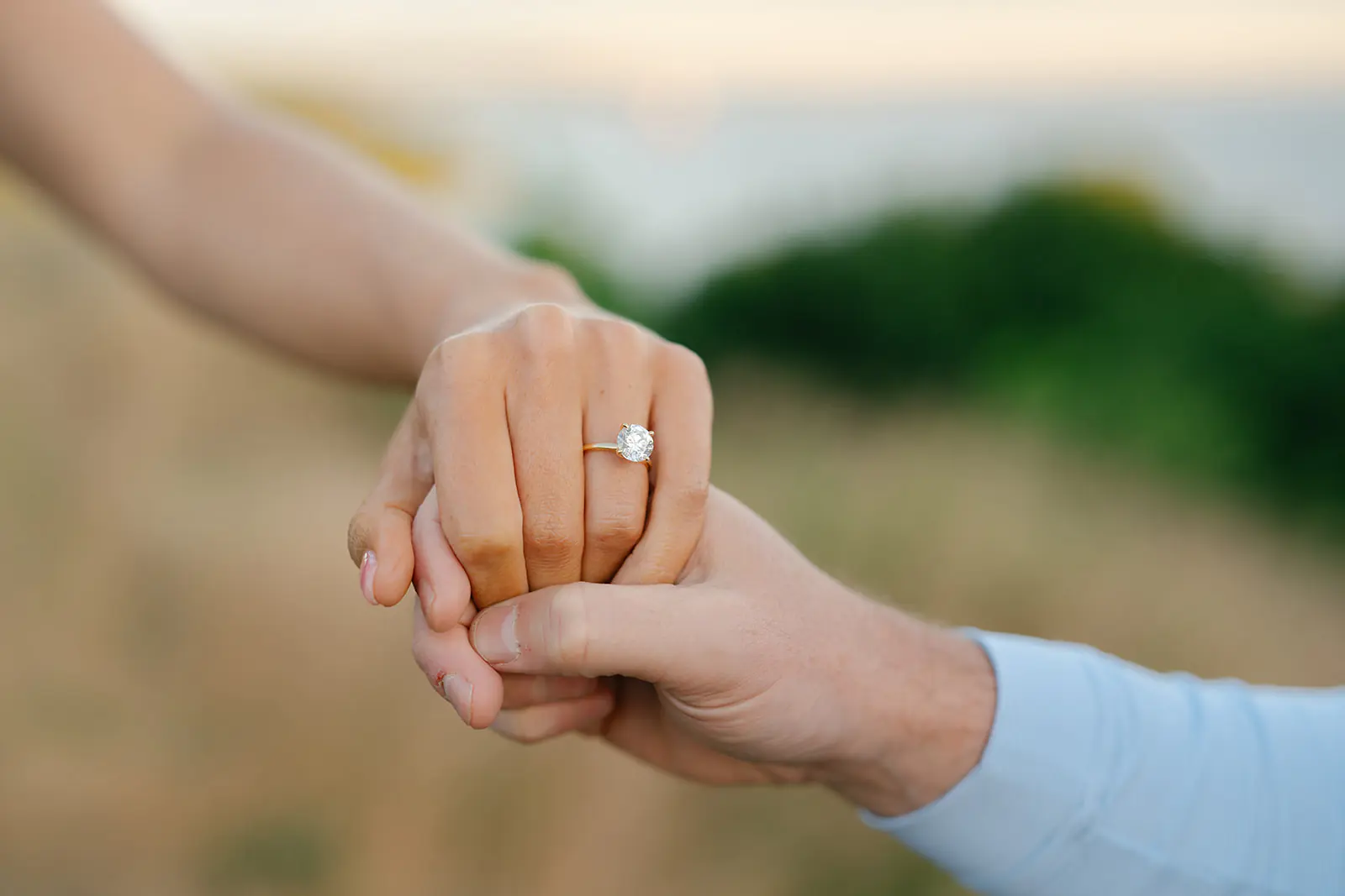 Close-up of clasped hands showing an engagement ring, water blurred behind them