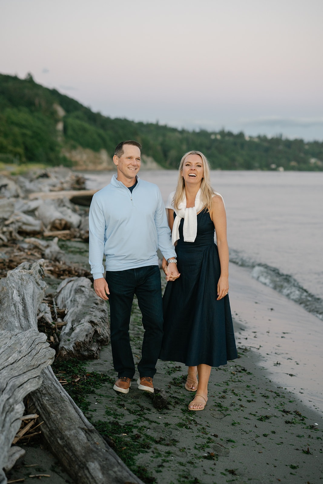 Couple laughs together on the beach beside piles of driftwood