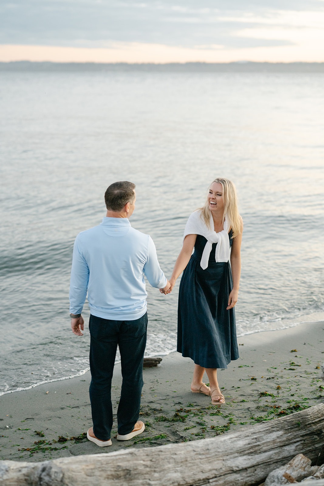 A quiet stretch of the field engagement session moves to the shoreline as the couple walks hand in hand