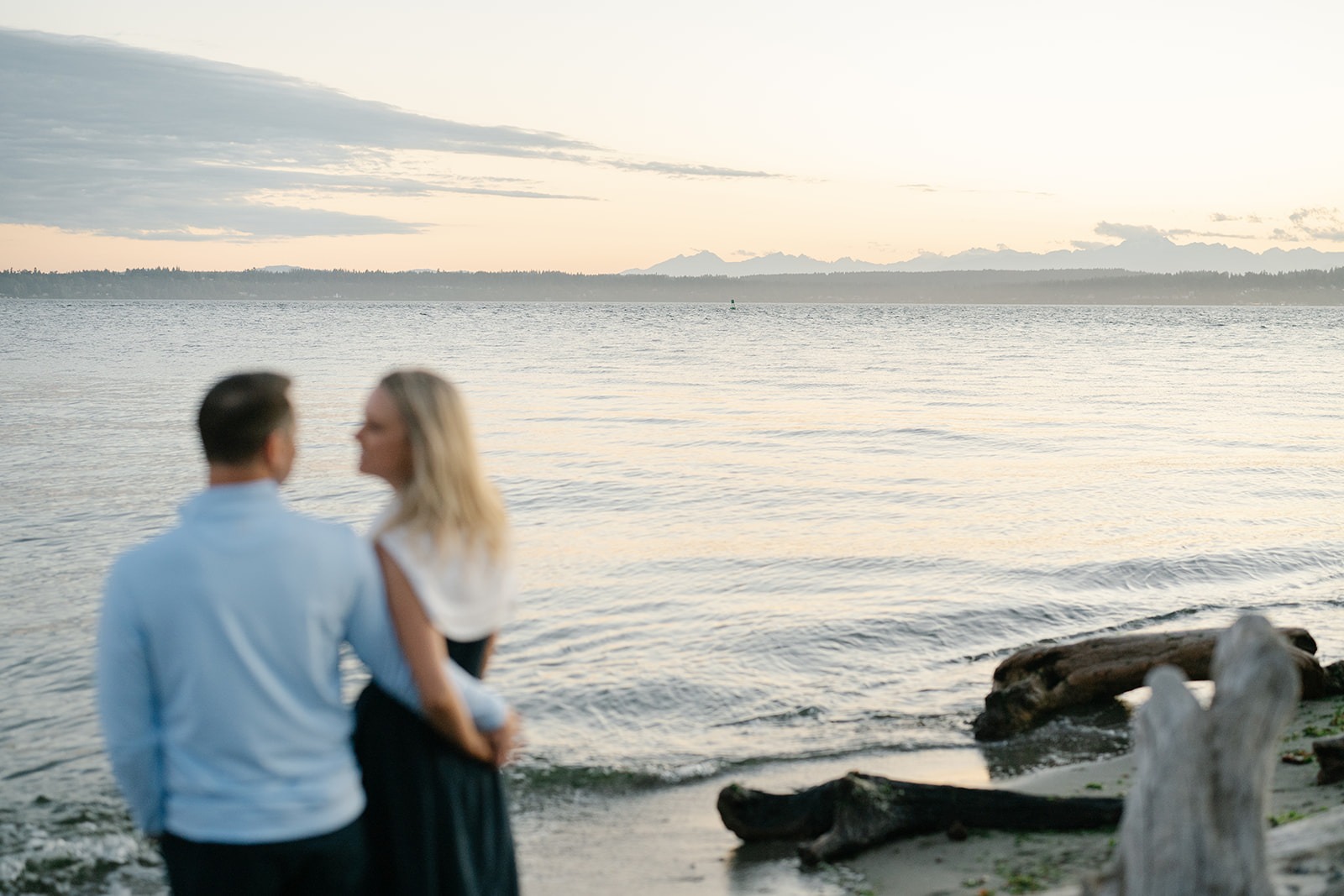 Couple stands together on a rocky beach shoreline as the sun sets