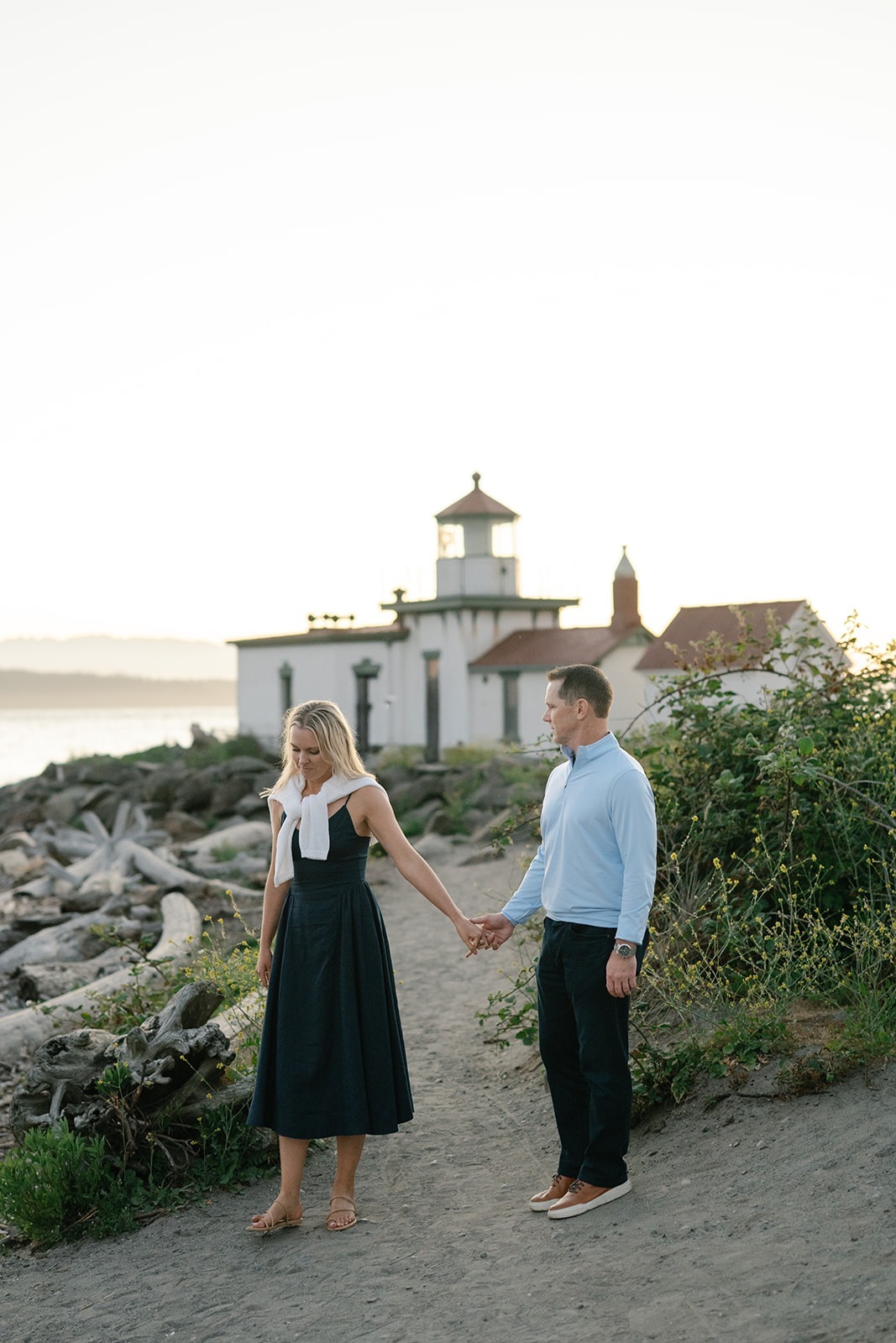 Couple walks a sandy path toward a small white lighthouse building
