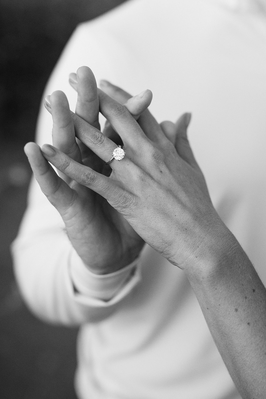 A black-and-white close-up shows clasped hands and an engagement ring