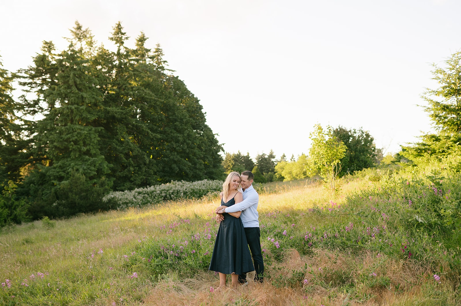 Couple embraces in a small clearing surrounded by wildflowers