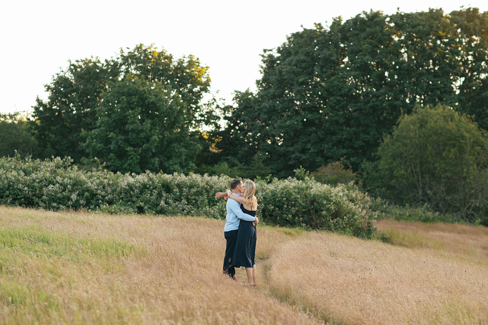 Wide view of the couple embracing on the grassy hillside during this field engagement session