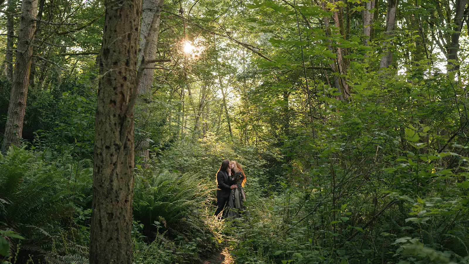 Couple embraces in a sunbeam-lit patch of forest