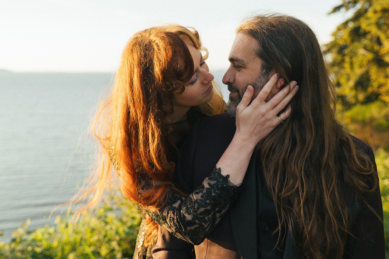 Bride rests her hand on the groom's cheek in a close portrait beside the water at golden hour