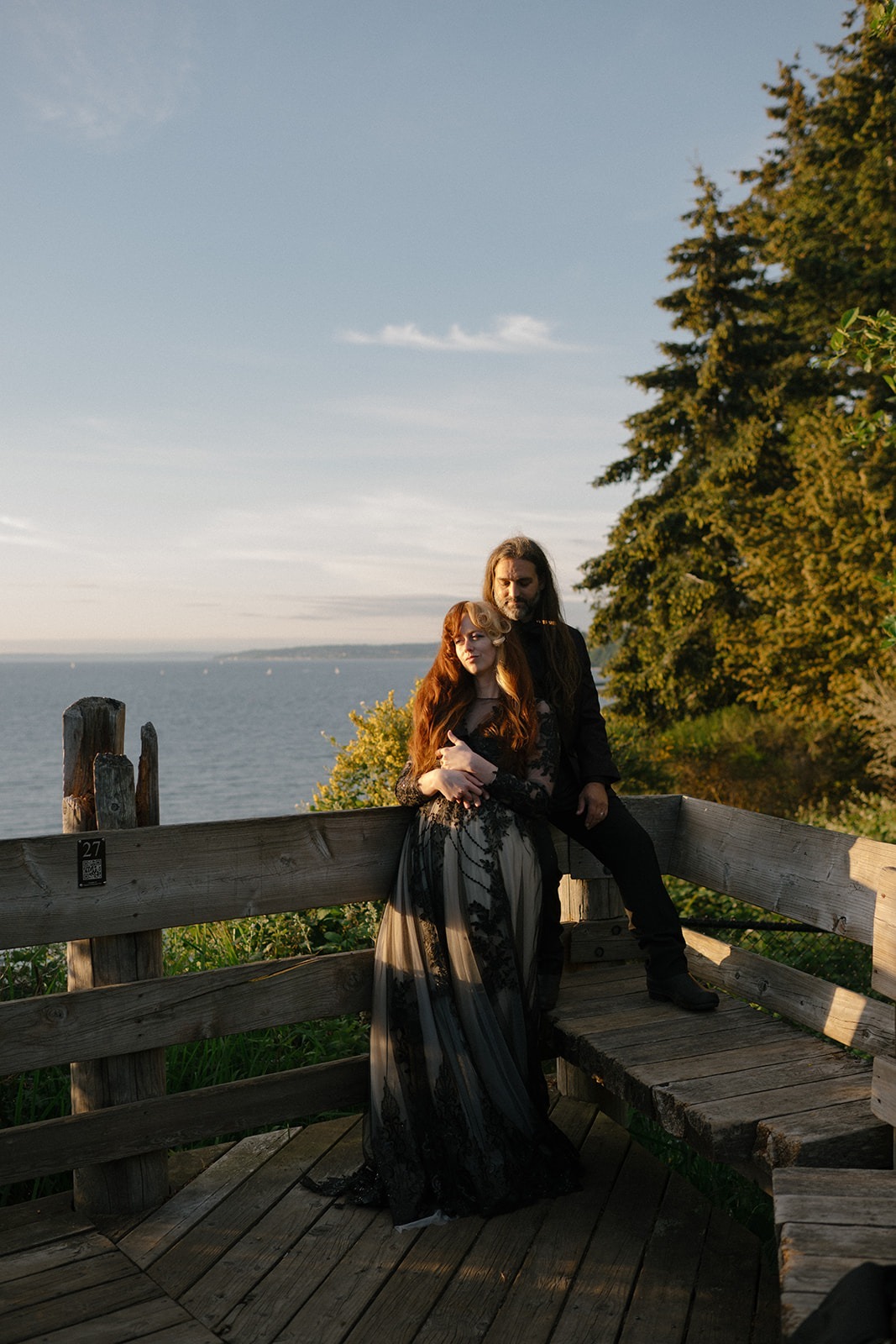 Couple stands together on a wooden boardwalk overlooking the water at dusk