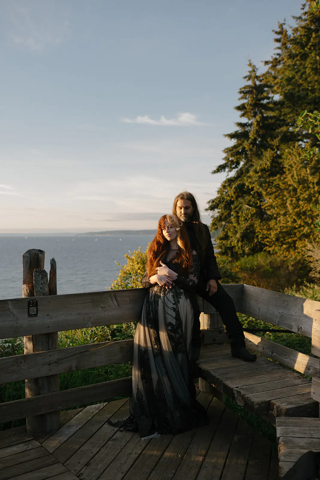 Couple stands together on a wooden boardwalk overlooking the water at dusk
