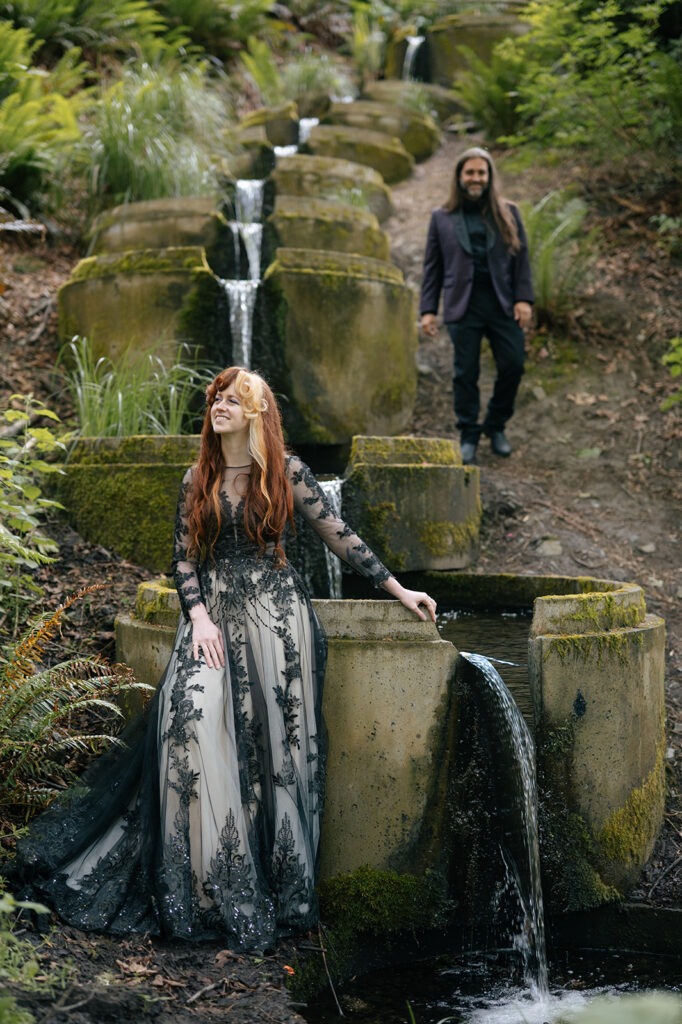This moody forest wedding portraits session found a hidden waterfall, bride resting a hand on the mossy stone