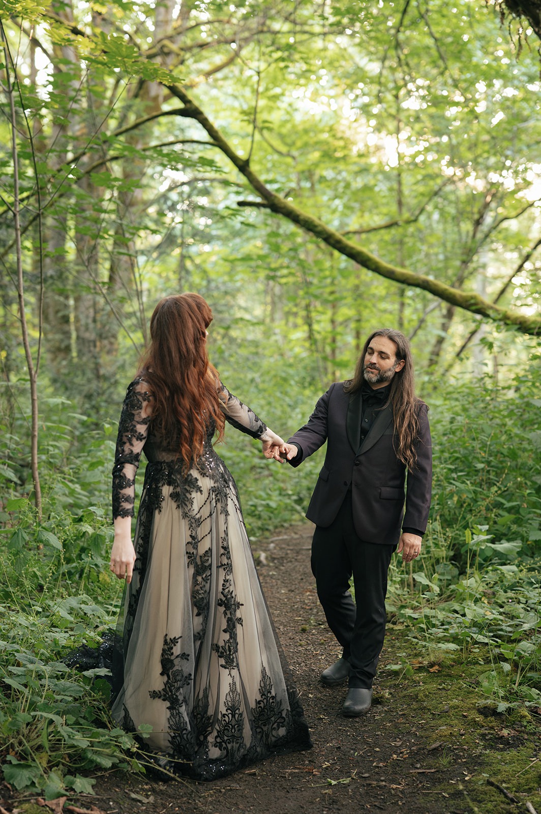 The bride leads the groom by the hand down a forest path