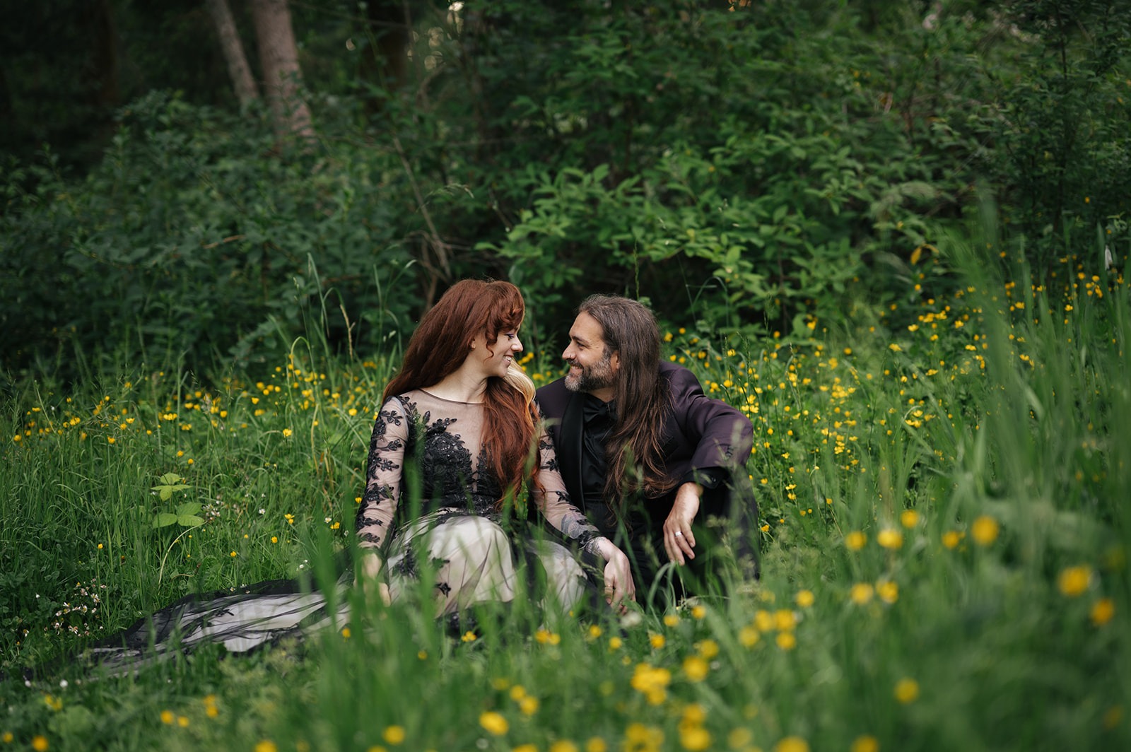 Couple sits together in a meadow dotted with small yellow wildflowers, bride leaning in for a kiss