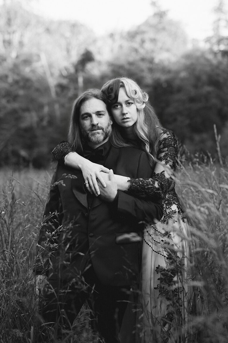 A black-and-white close-up captures the couple embracing in a field of tall grass