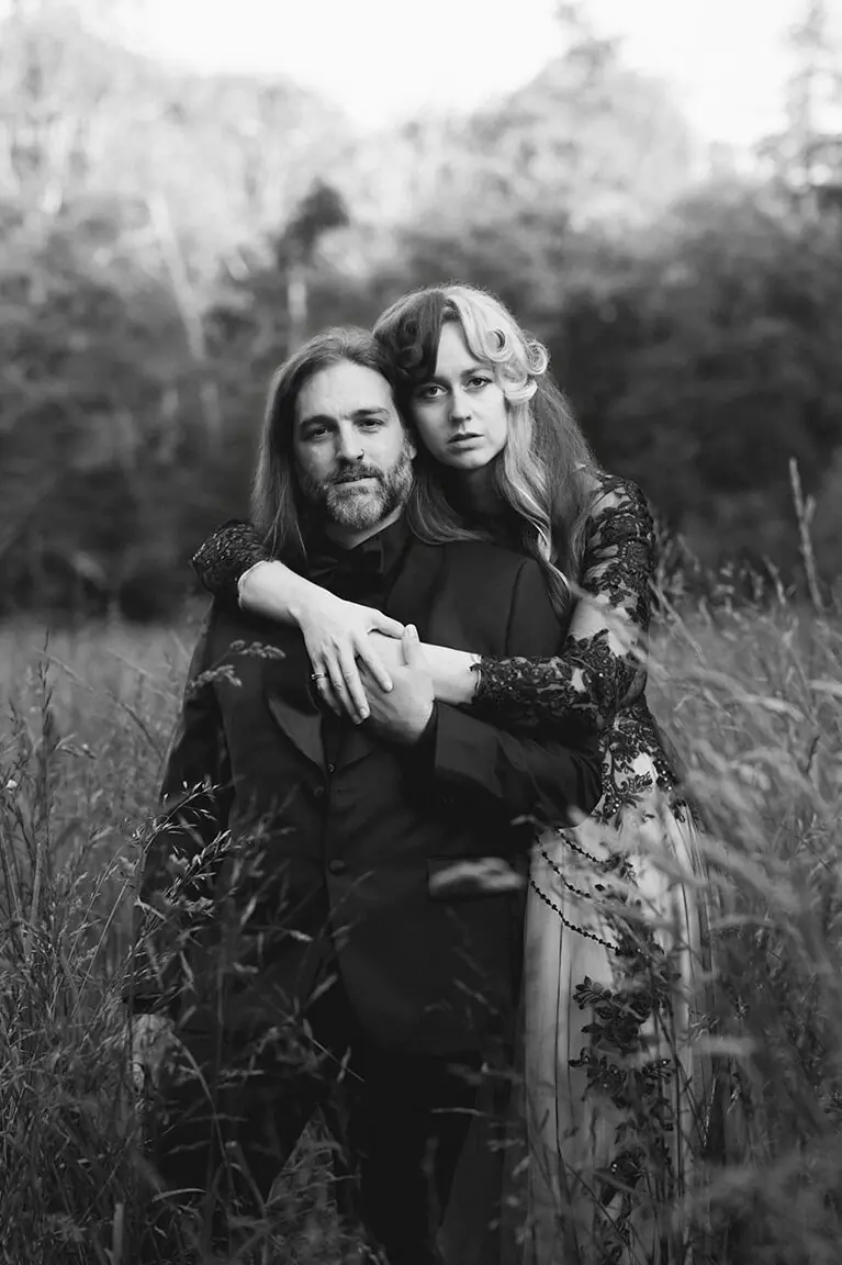 A black-and-white close-up captures the couple embracing in a field of tall grass