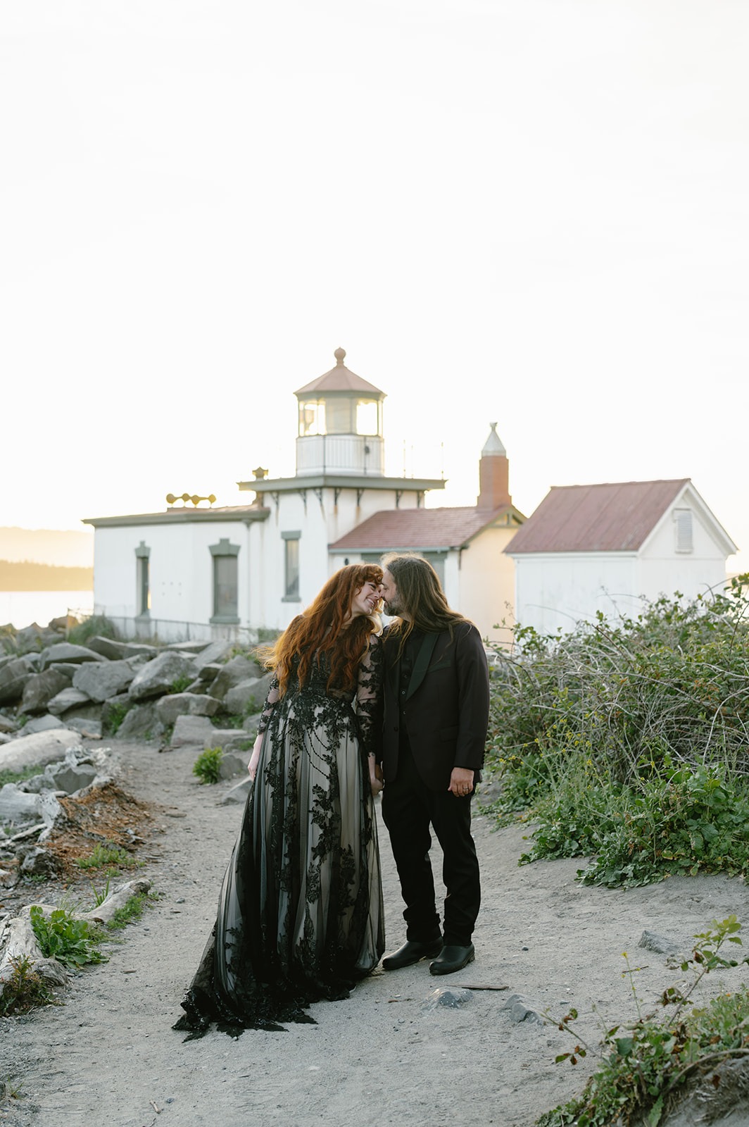 Couple walks a sandy path toward a small white lighthouse