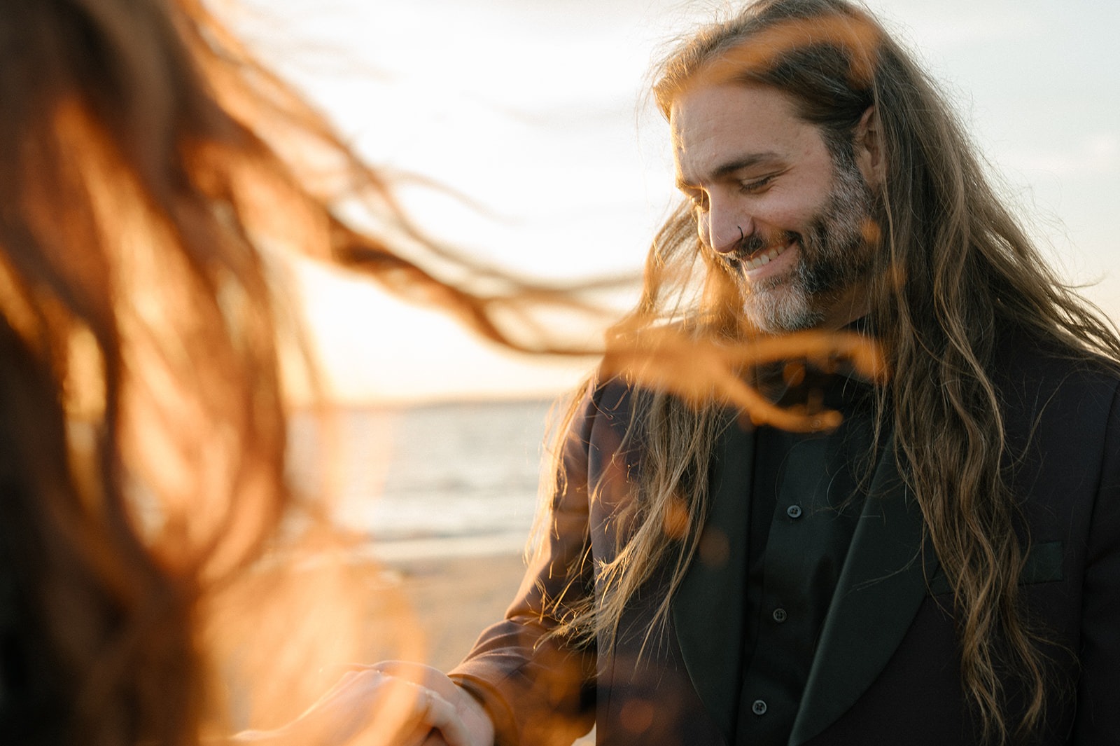 Groom laughs as his long hair blows across his face in the wind