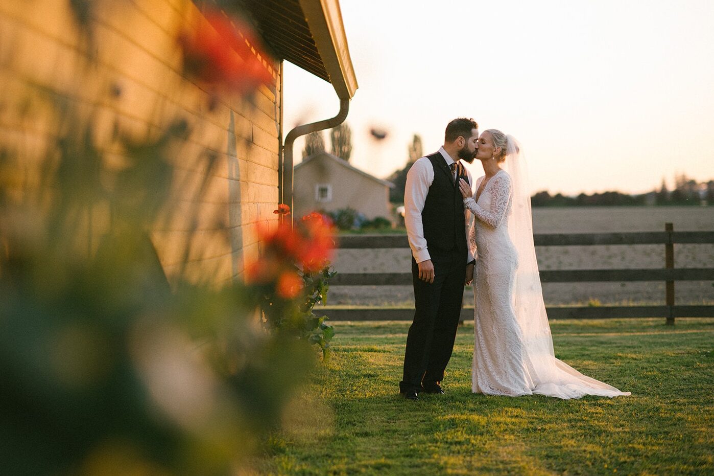 Bride and groom share a kiss beside the barn as golden light fades