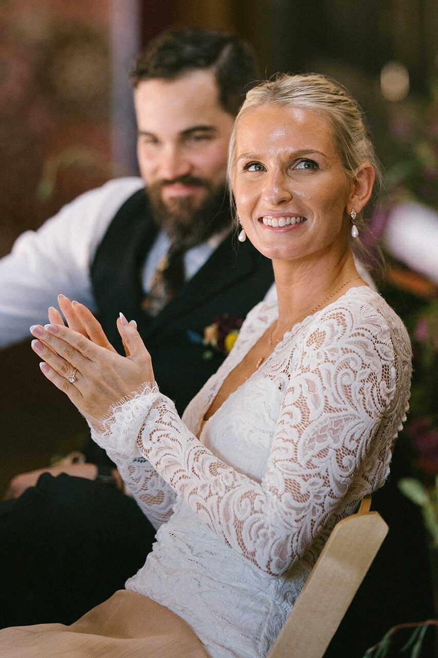 Bride claps and laughs while the groom smiles beside her at the head table